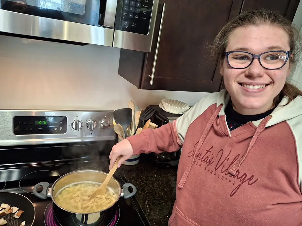 A participant smiling while stirring a pot of pasta on the stove
