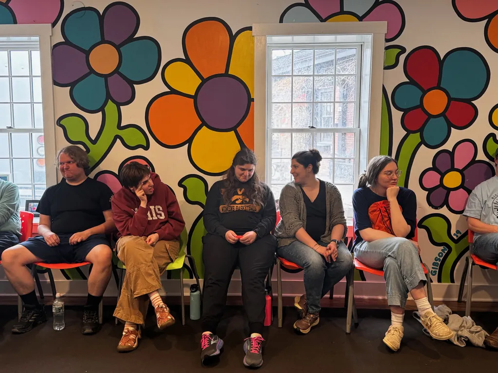 Participants and staff sitting together in a row of chairs in front of a colorful flower mural