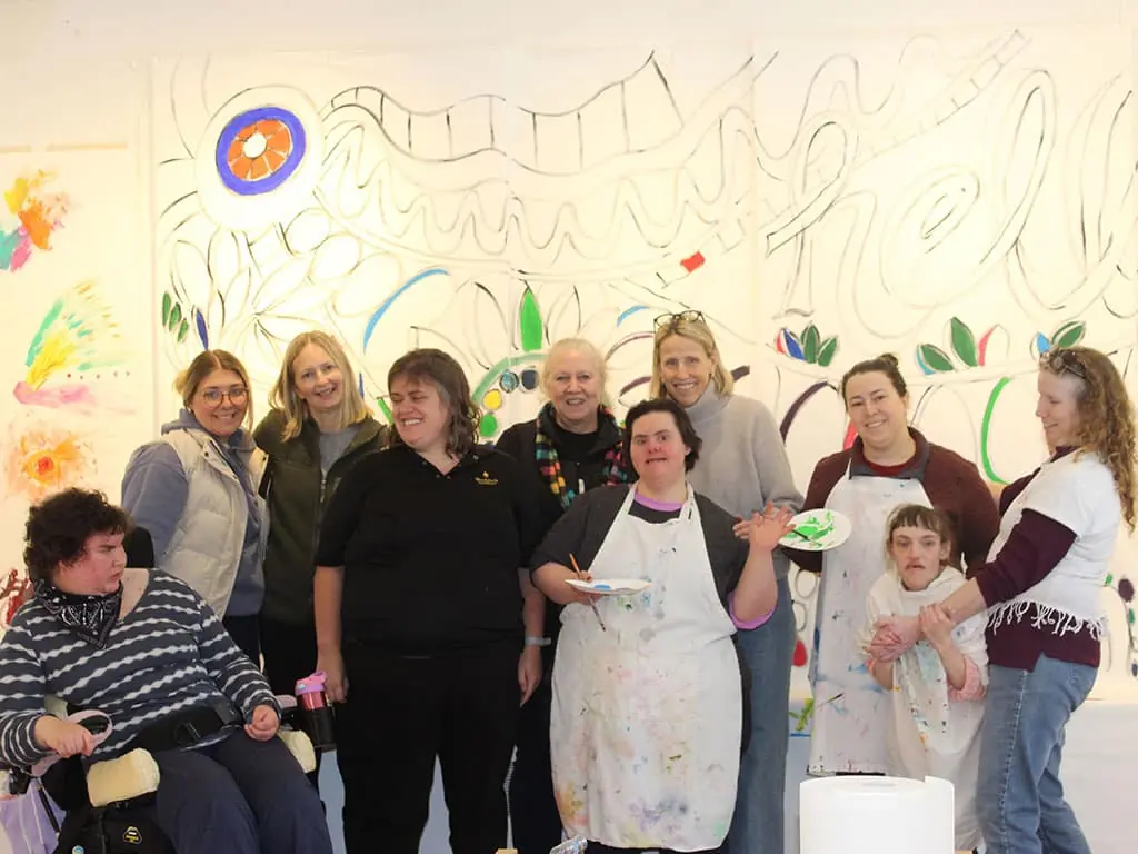 Participants and artists gathered in front of a large mural in progress