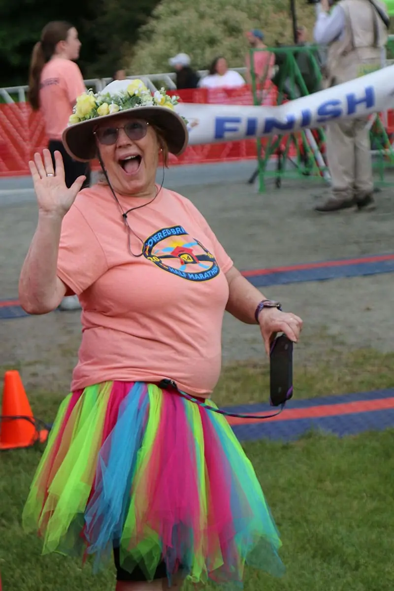 A cheerful runner in a flowered hat and rainbow tutu waving near the finish line