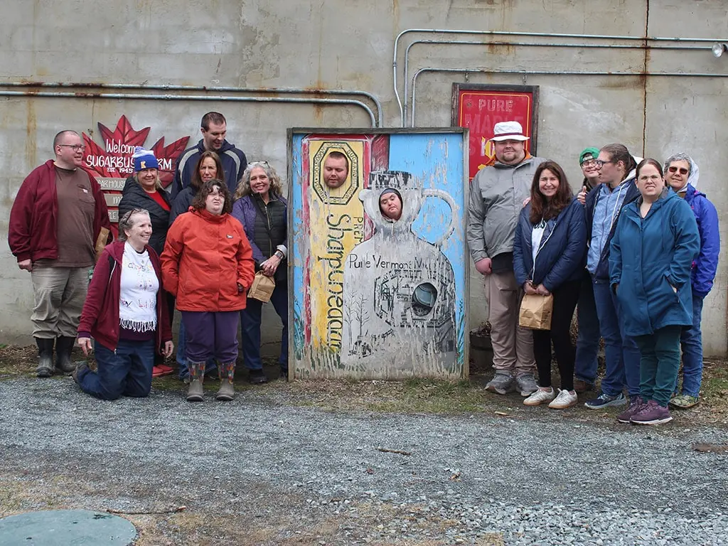 Participants and staff posing with a painted cutout board at a sugarhouse