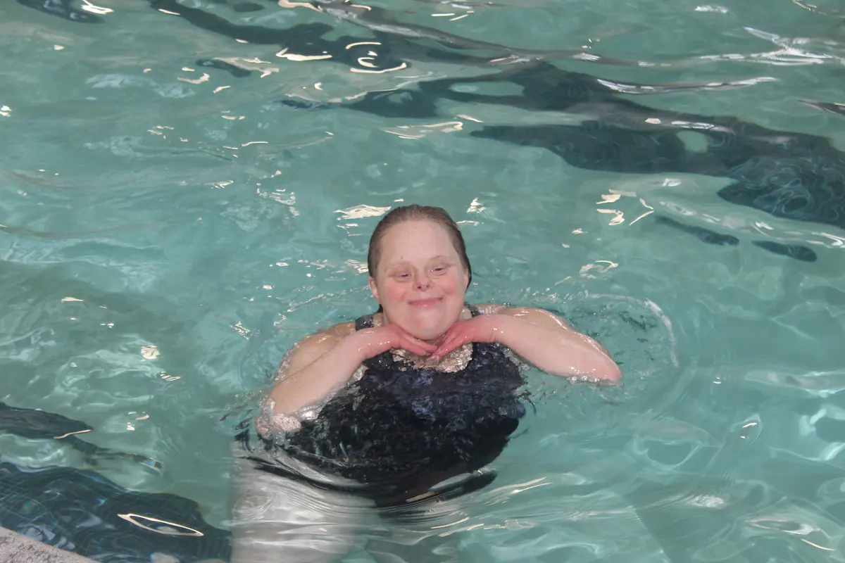 A smiling participant swimming in the pool with her chin resting on her hands
