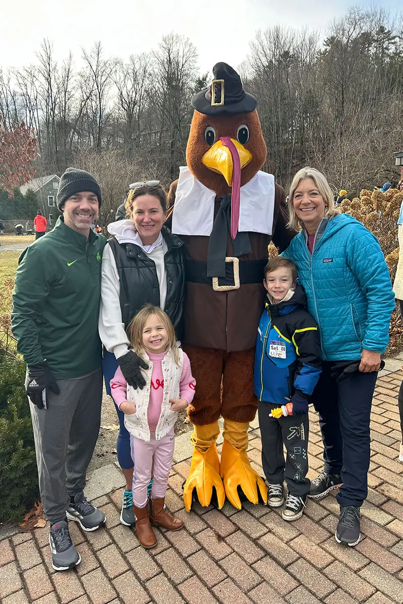 A family posing with the Turkey Trot turkey mascot